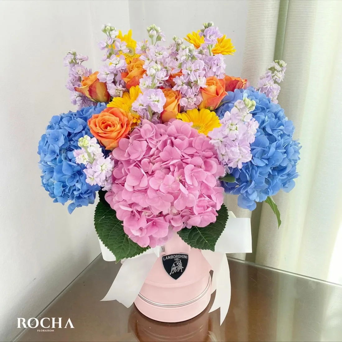 Pastel arrangement of hydrangeas, roses and gerberas in a pink hat-box